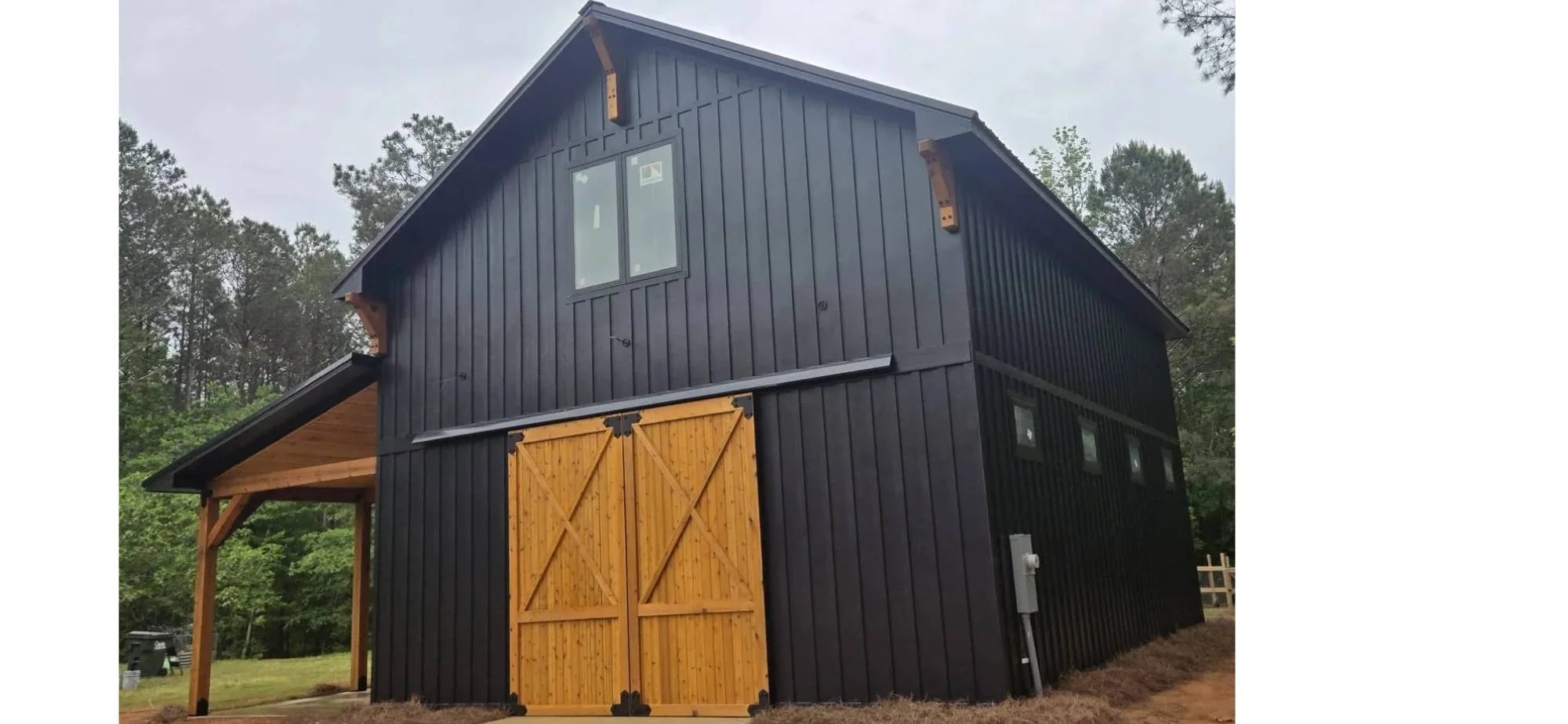 Black metal siding on modern barn structure with wood doors and timber overhang