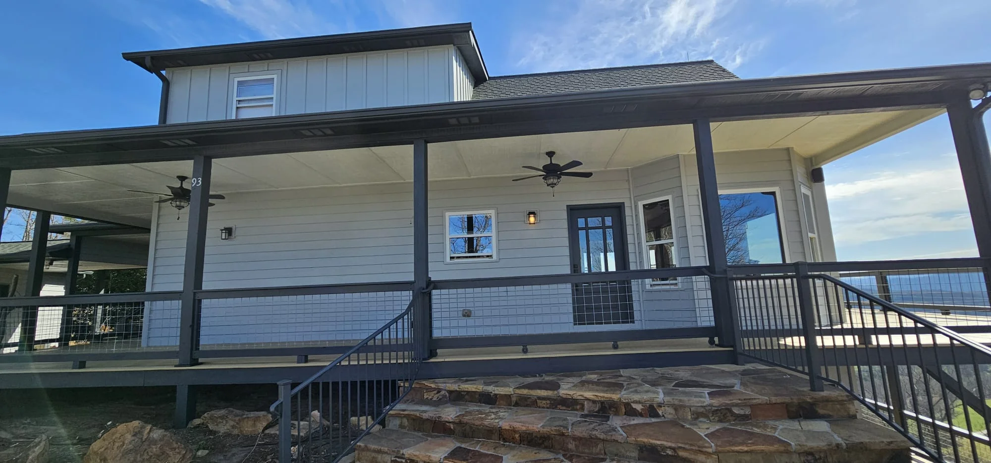 Modern farmhouse with large windows, covered metal porch, and cable railings