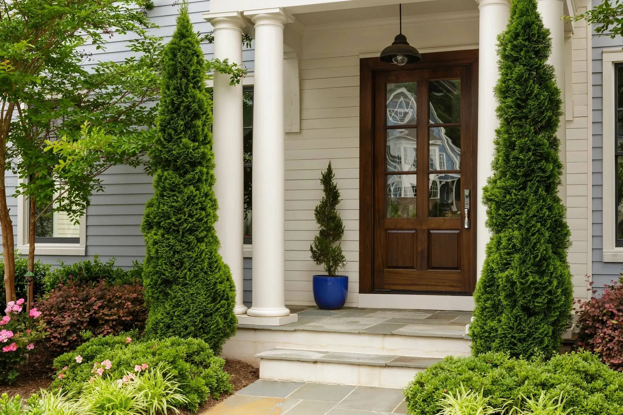 Dark wood entry door with glass panels on white columned portico with stone steps