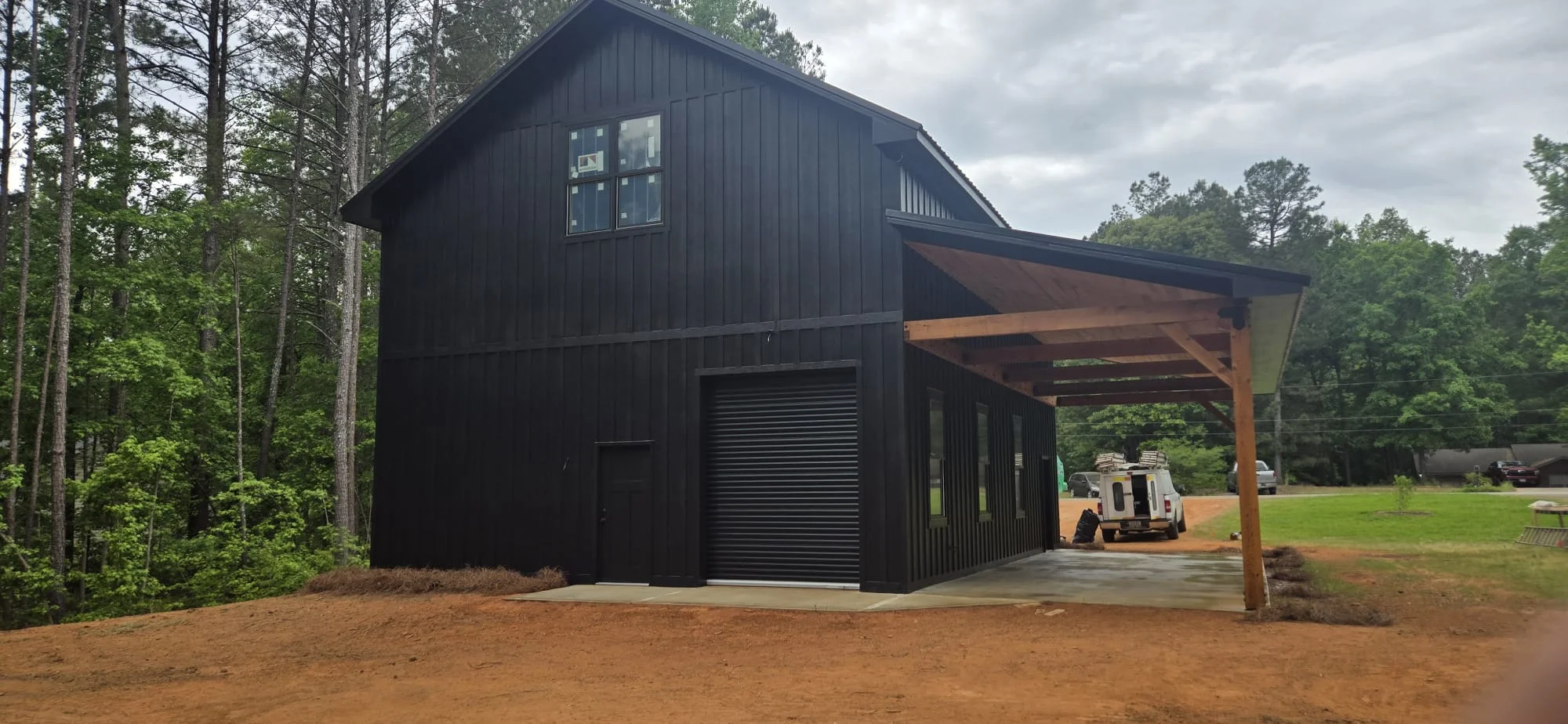 Black metal barn with casement windows and wood pergola carport on rural property