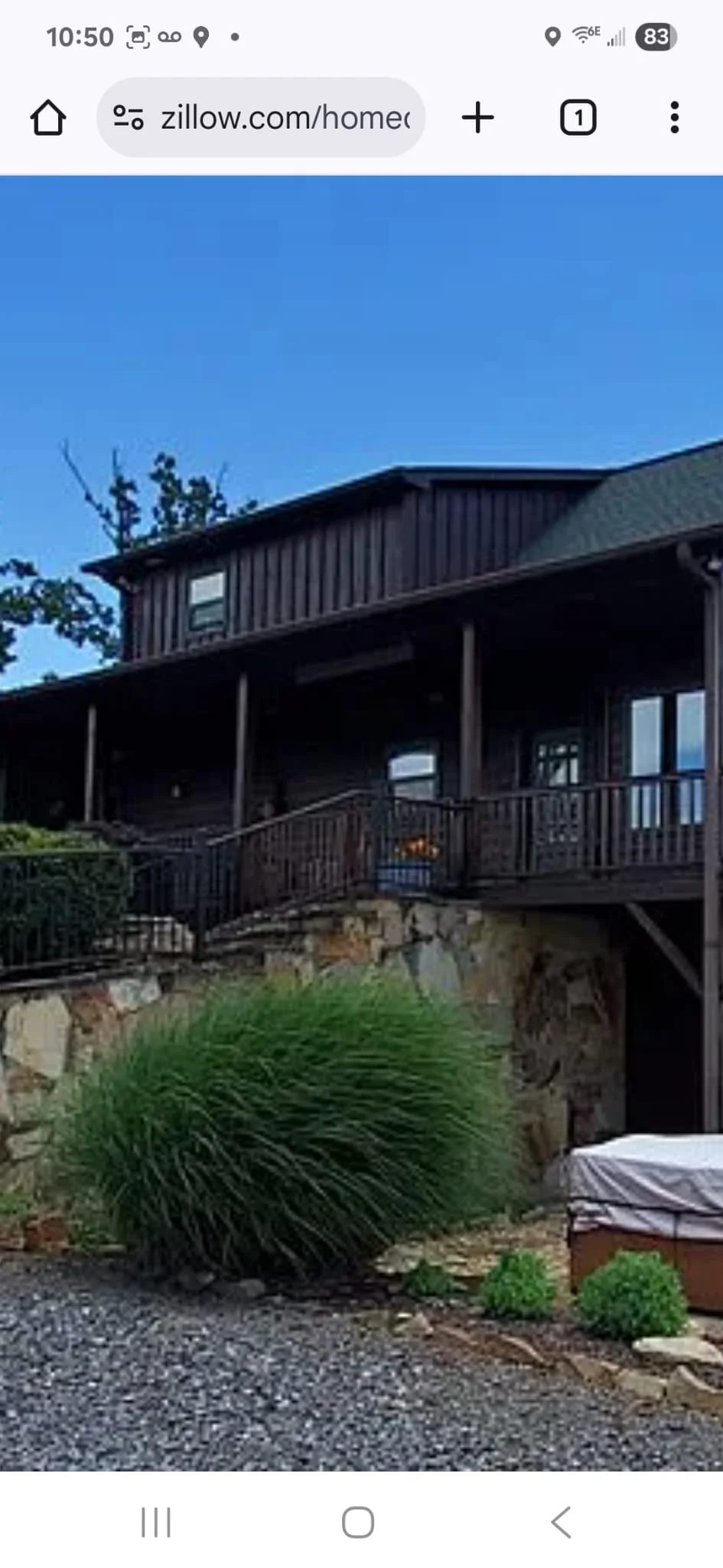 Modern home with dark metal siding, large windows, stone foundation, and landscaping