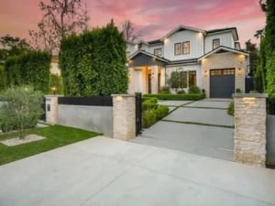 Modern two-story home with stone pillars, architectural windows, and manicured landscaping at dusk