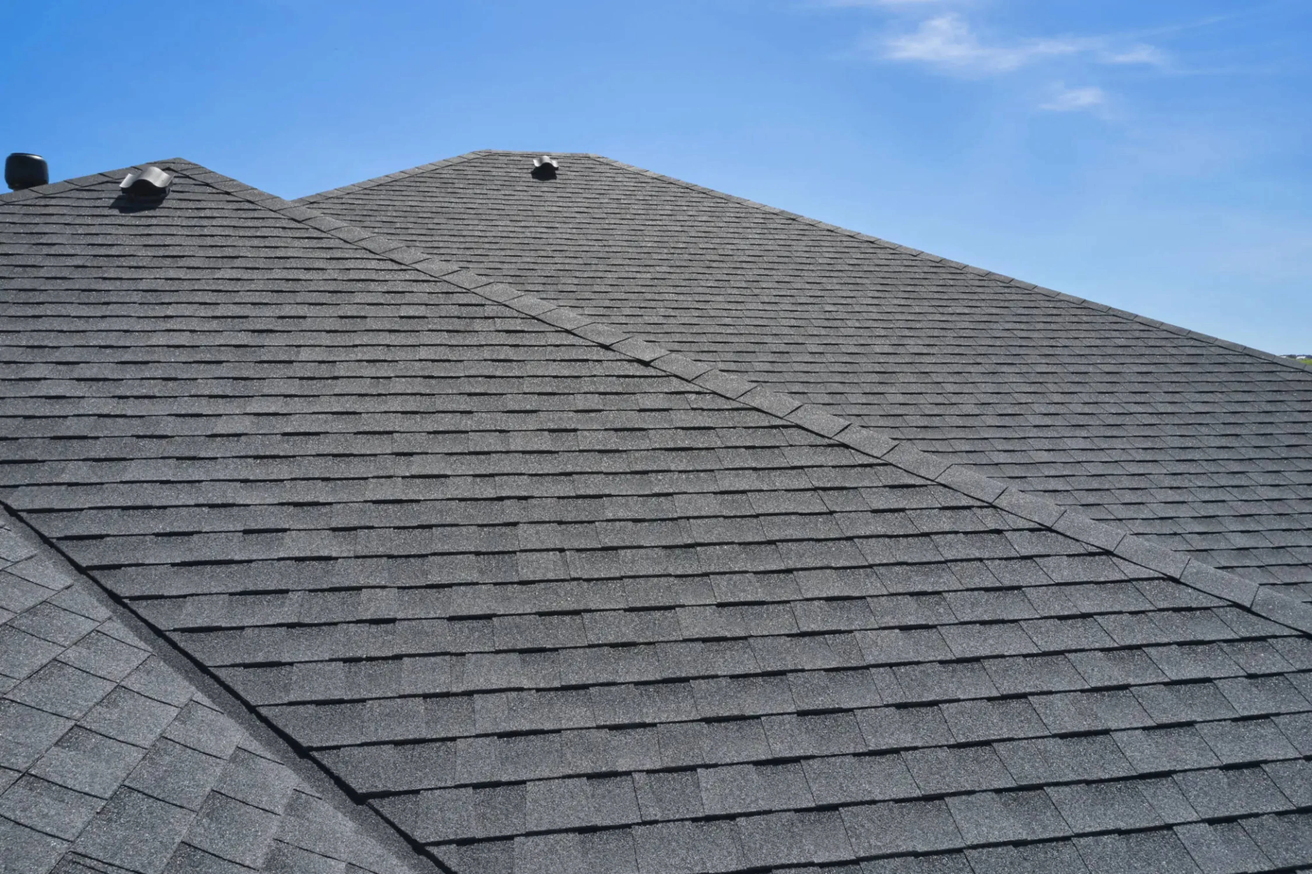Newly installed gray architectural shingles on pitched residential roof with clear blue sky