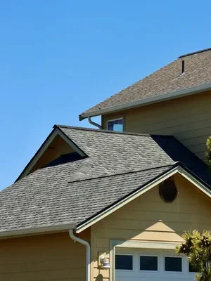 Two-story home with new gray asphalt shingle roof and installed gutters against clear blue sky
