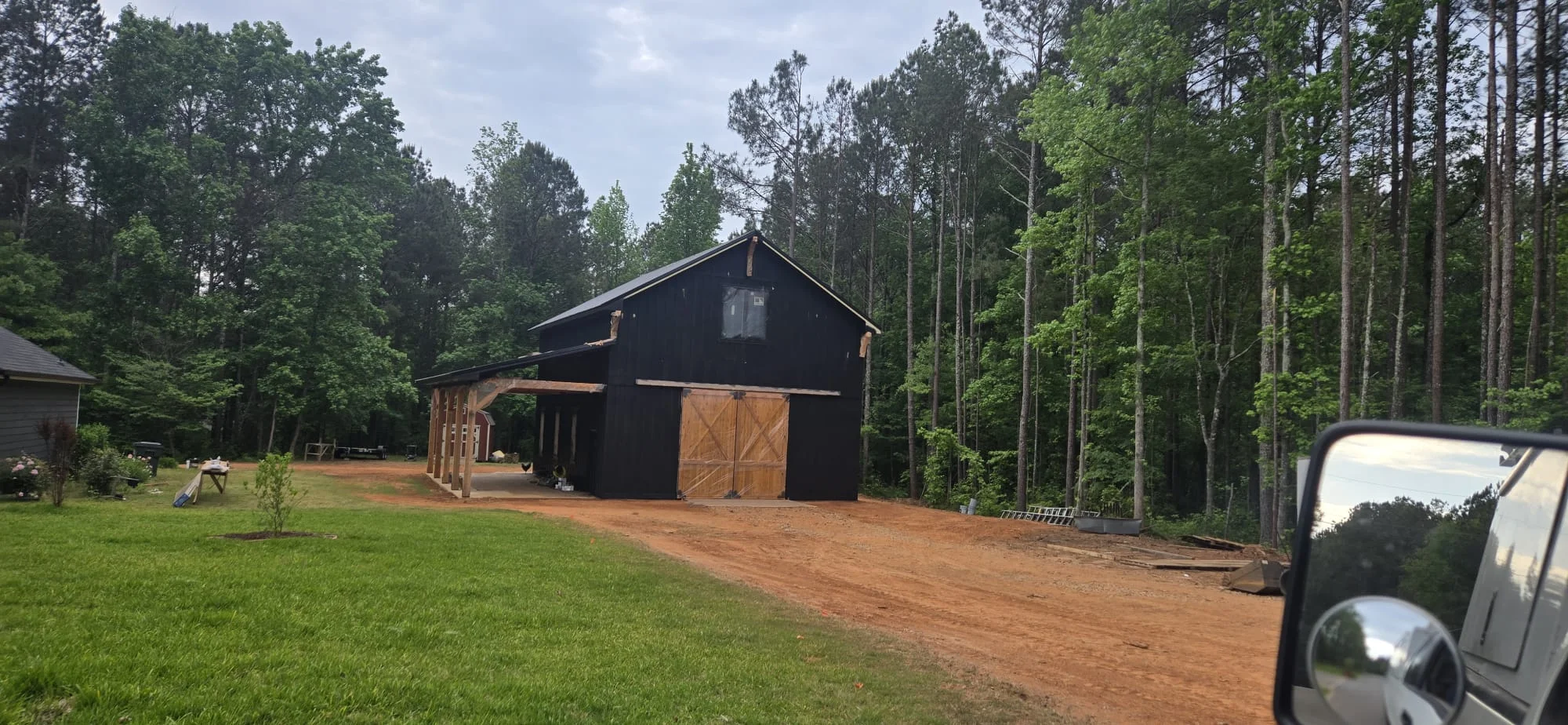 Black barn with new windows, wood doors, and covered porch surrounded by tall pines