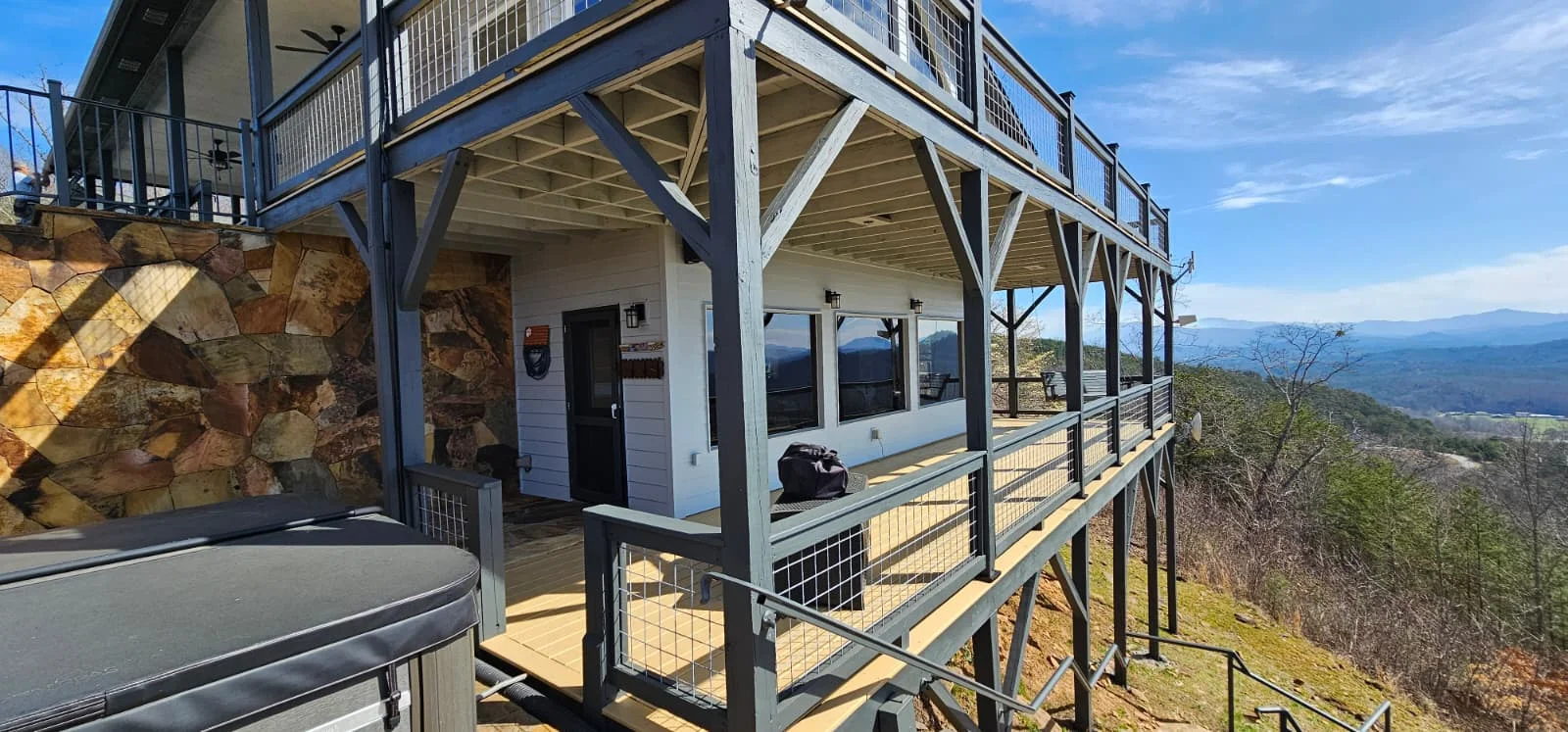 Modern mountain home with large windows, elevated deck, and cable railings overlooking valley landscape