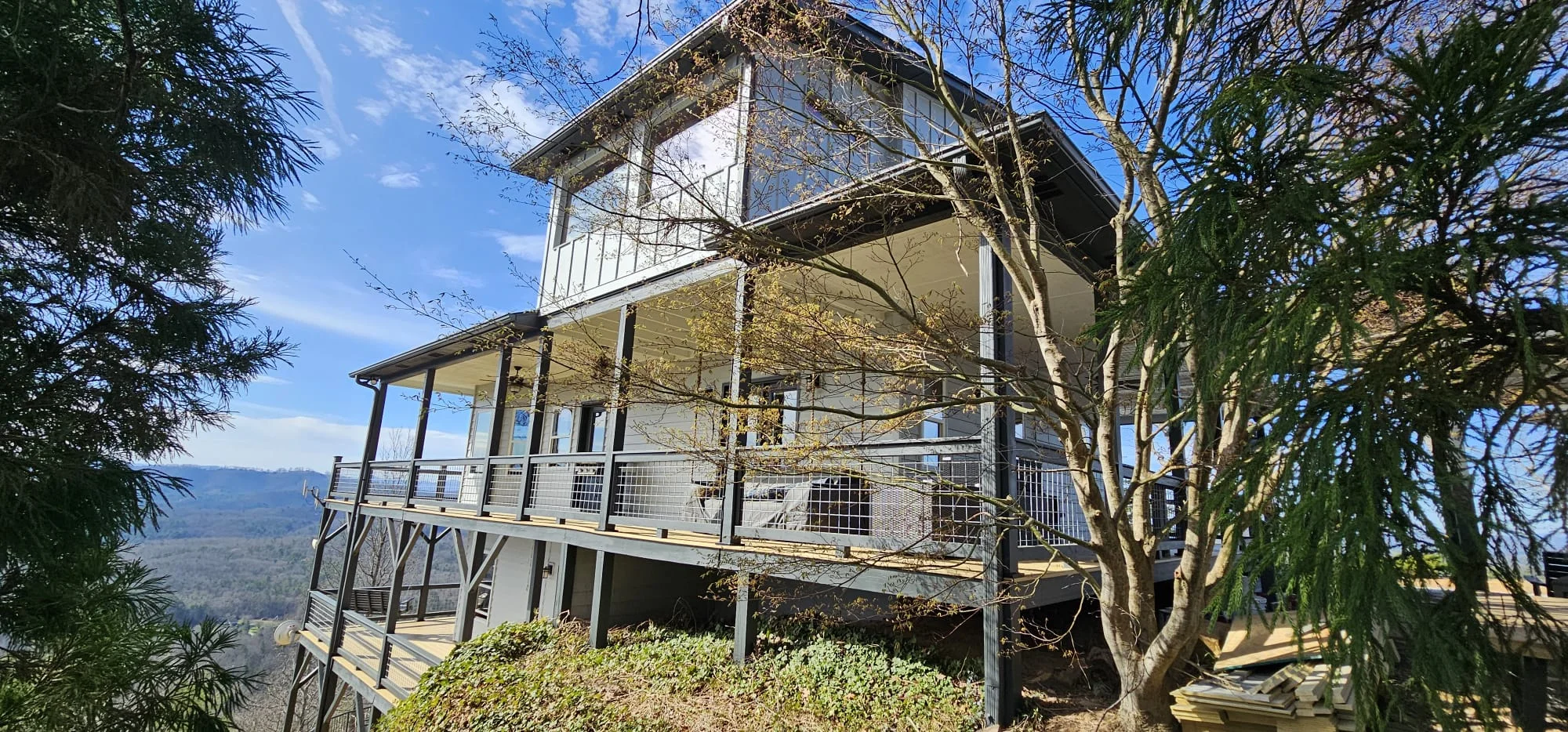 Modern elevated home with extensive window installation and metal deck railings overlooking valley landscape