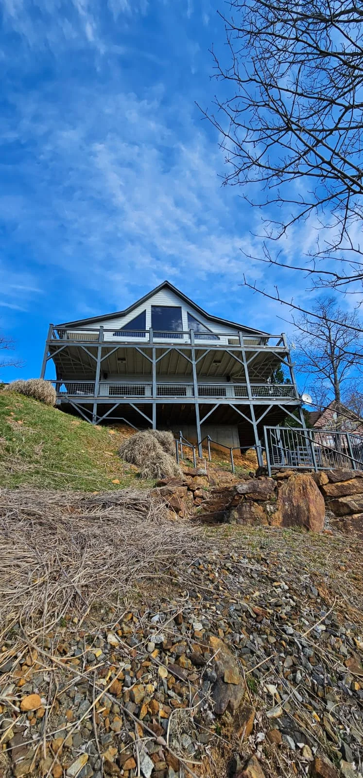 Modern hillside home with new white windows, metal railings, and wooden support beams